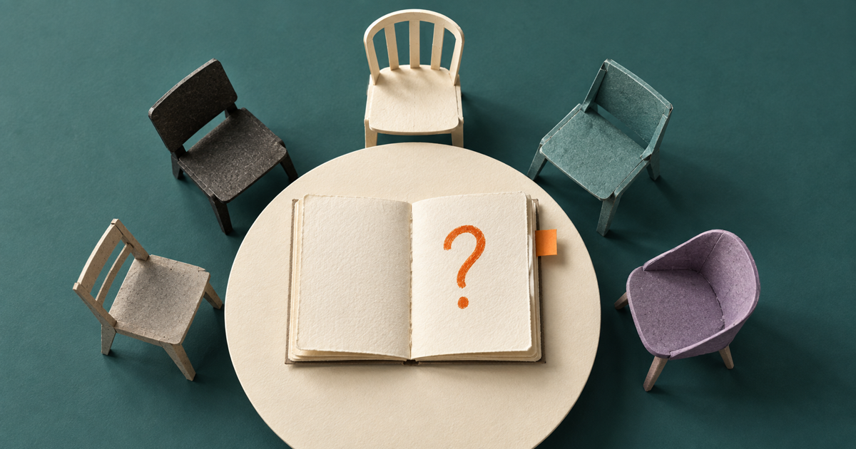 Five handcrafted paper chairs surround an open notebook with an orange question mark, representing a personal board of advisors around one decision.